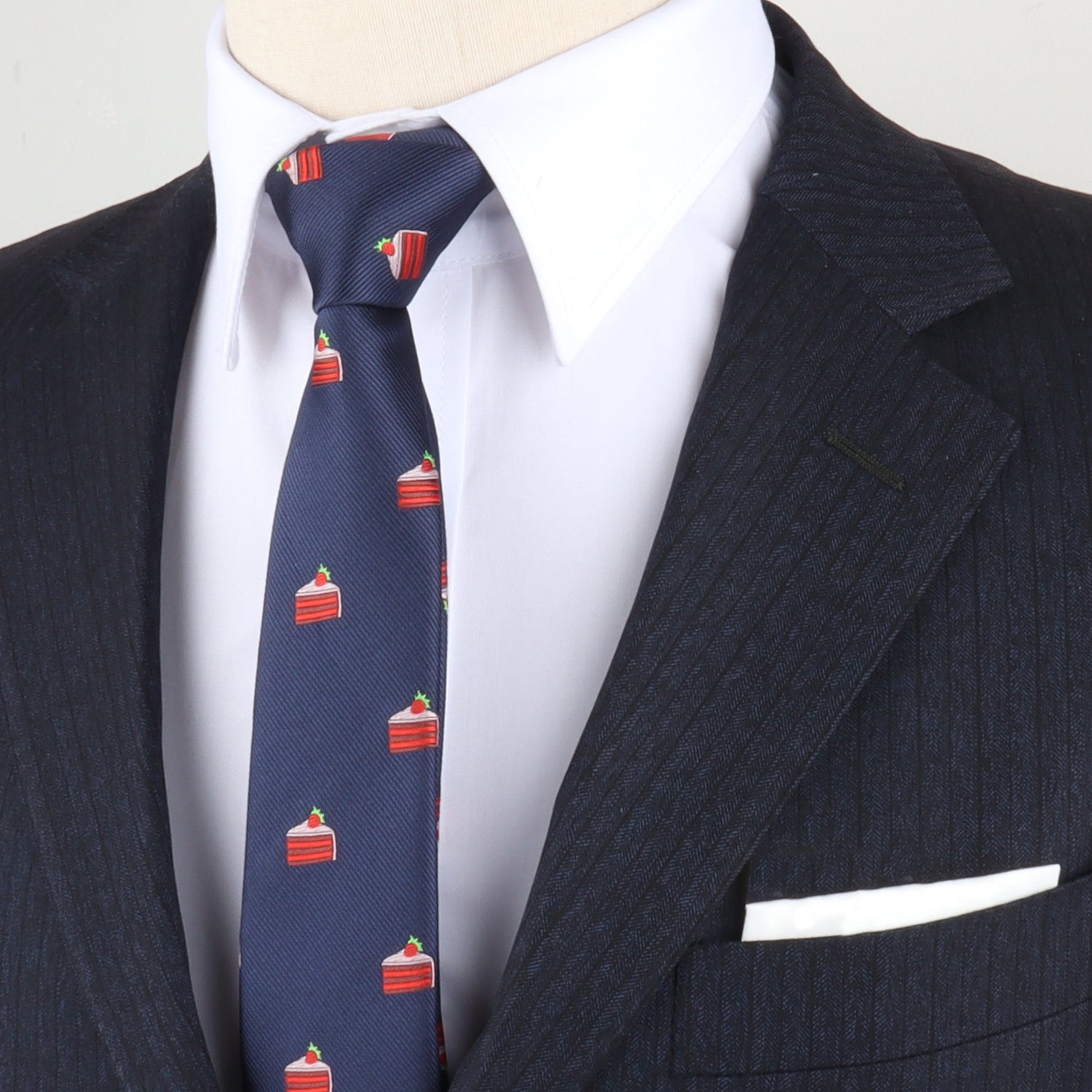 A person dressed in a dark pinstripe suit, white dress shirt, and the Strawberry Cake Skinny Tie—featuring red cake slice motifs—completes the look with a crisp white pocket square.