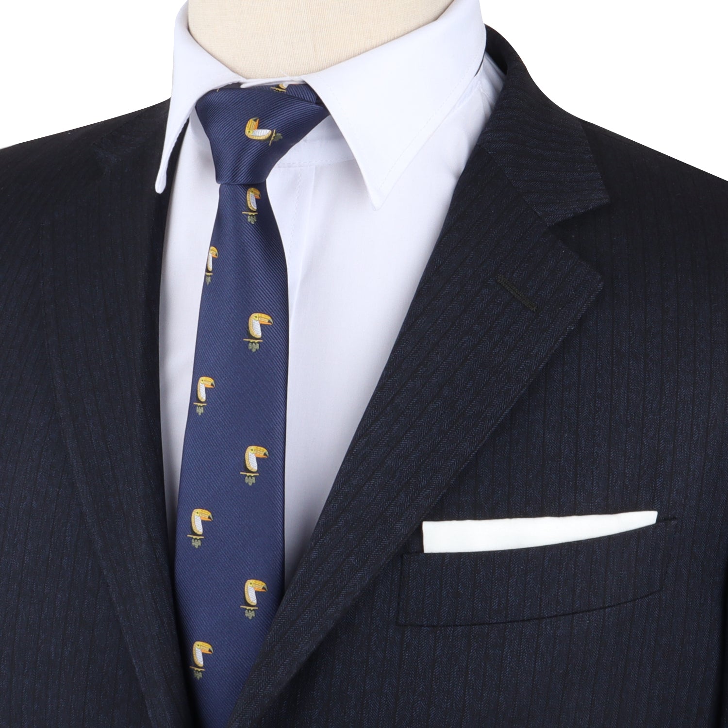 A mannequin sports a dark pinstripe suit, white shirt, crisp white pocket square, and the Toucan Bird Skinny Tie—blue with a repeating yellow toucan pattern—making it an ideal gift for bird lovers.
