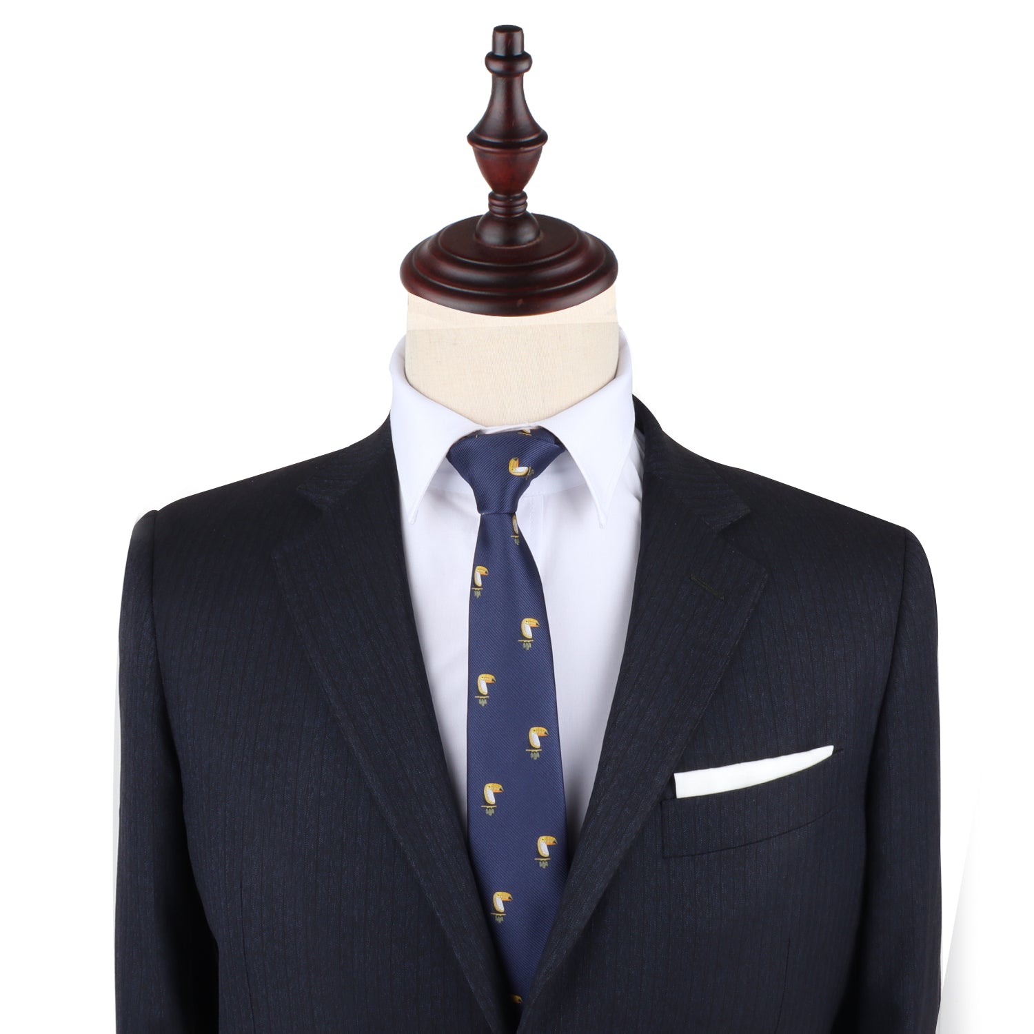 A dark suit jacket, white dress shirt, and Toucan Bird Skinny Tie are displayed on a mannequin with a wooden stand; a white pocket square adds flair—making this tie a perfect unique gift for bird lovers.