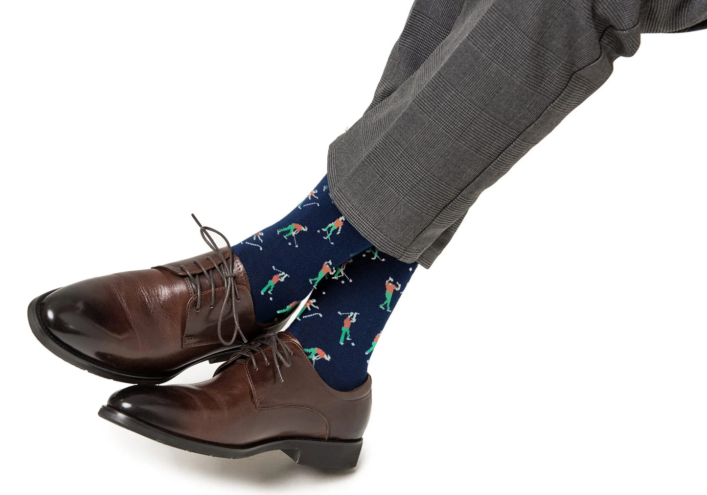 A man showcases his socks, the Angry Golfer Socks, with a colorful golfer pattern that adds a sporty flair to his brown dress shoes and gray trousers.