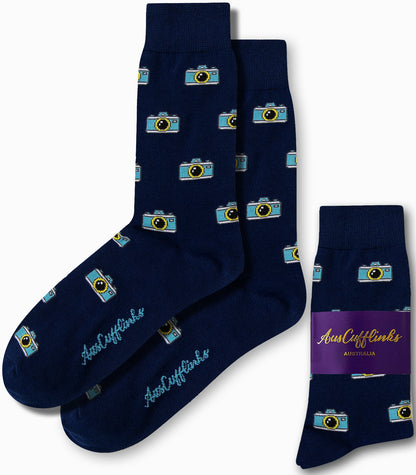 Neatly folded and packaged, the Camera Socks feature a stylish navy blue design adorned with a camera pattern, all wrapped up with a touch of flair thanks to their vibrant purple label.