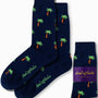 The Palm Tree Socks in navy blue feature scattered green and orange palm tree patterns that evoke tropical vibes, and are perfectly complemented by their matching packaging.