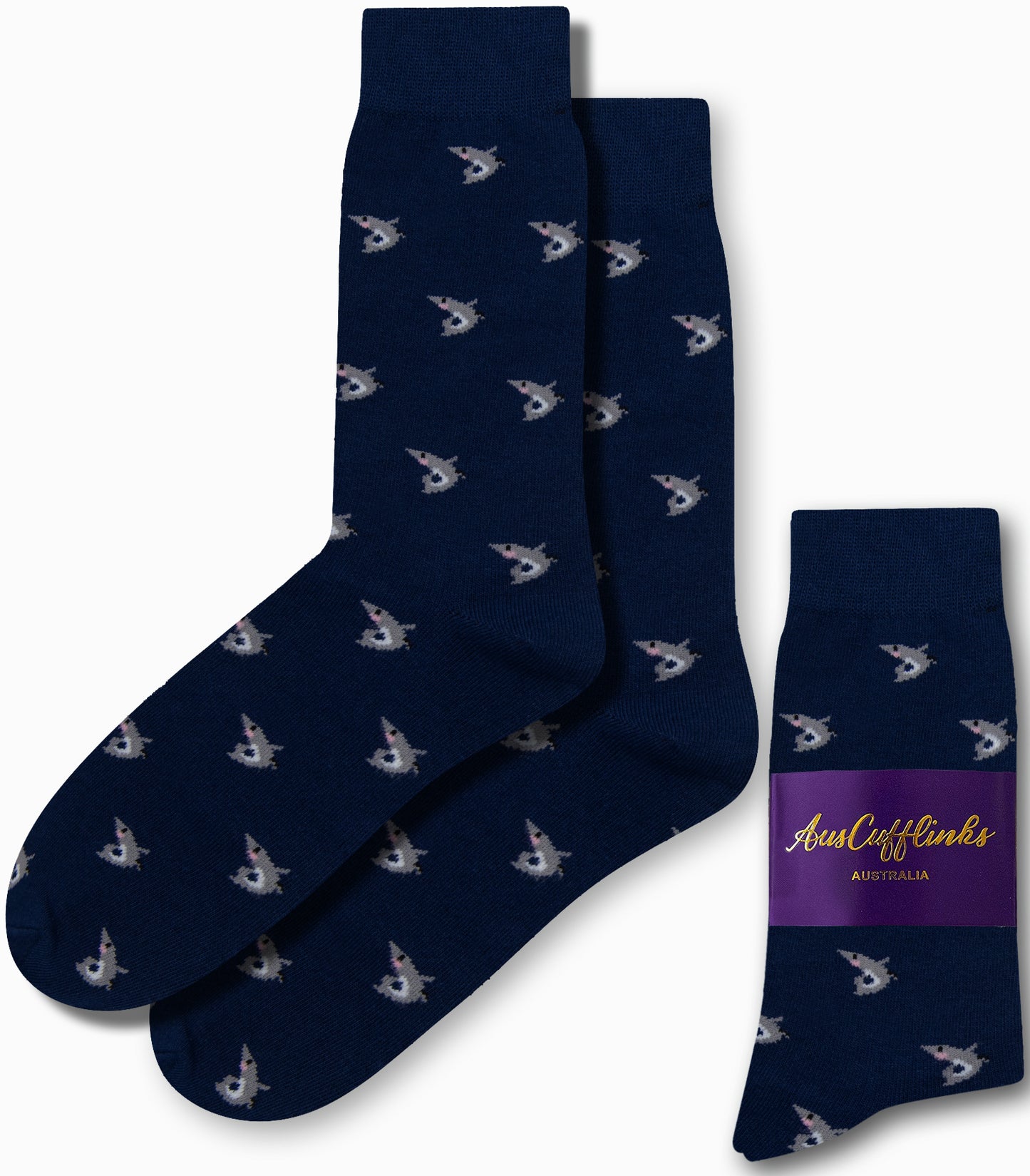 Navy blue socks showcasing a pattern of small, white shark faces bring a touch of deep-sea style to your wardrobe. Packaged with a purple label reading "AusCufflinks Australia," these socks add a unique flair perfect for any fashion dive.