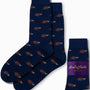 The Triceratops Socks in navy blue display a stylish pattern of brown triceratops dinosaurs, offering a touch of prehistoric elegance and are elegantly packaged with a purple label.