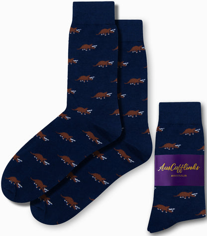 The Triceratops Socks in navy blue display a stylish pattern of brown triceratops dinosaurs, offering a touch of prehistoric elegance and are elegantly packaged with a purple label.