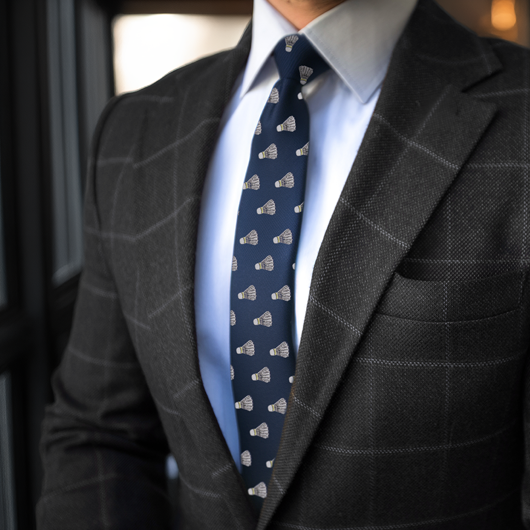 A person in a dark plaid suit and light blue dress shirt serves looks with a Badminton Skinny Tie.