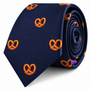 Introducing the Bagel Skinny Tie—a navy blue necktie featuring an embroidered orange bagel pattern, elegantly rolled and set against a white backdrop. Ideal for food enthusiasts seeking a quirky accessory or anyone with a taste for bagel-inspired designs.