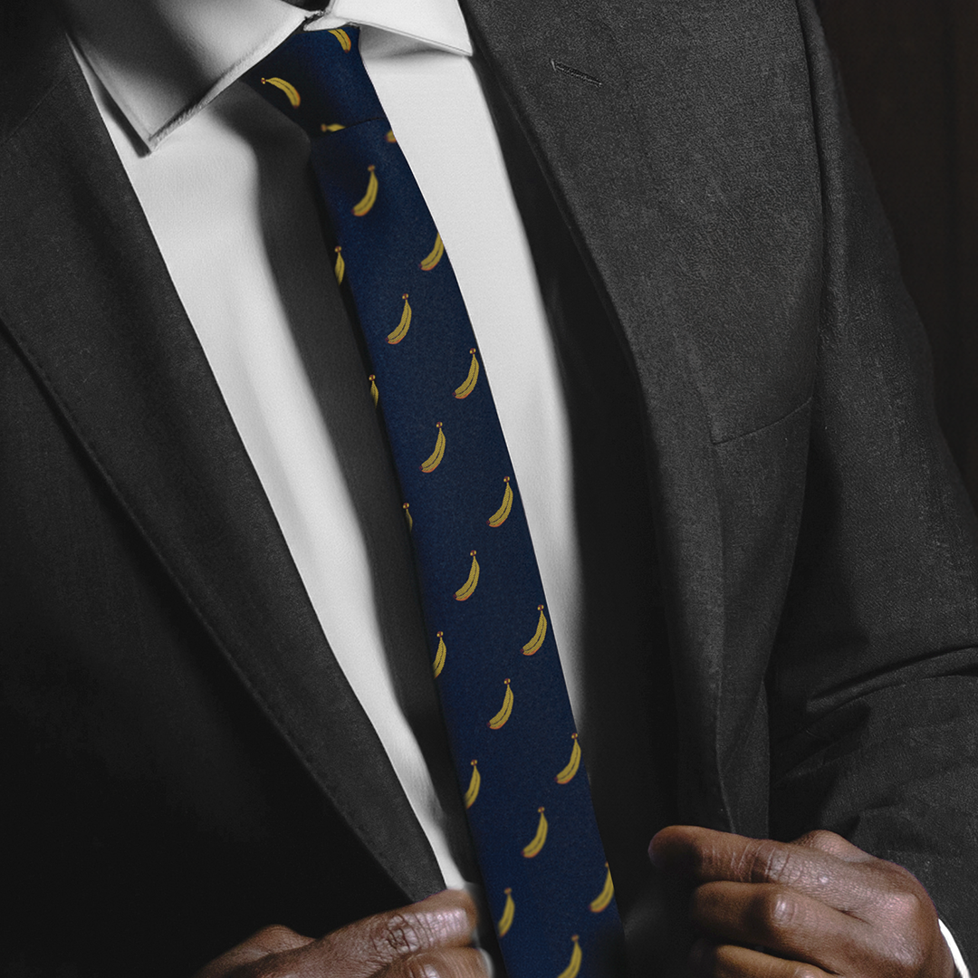 A person adjusts a dark suit jacket, revealing a white shirt and a Banana Skinny Tie, embodying modern elegance.