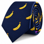 A Banana Skinny Tie in navy blue, featuring a yellow banana print pattern, rolled up on a white background.