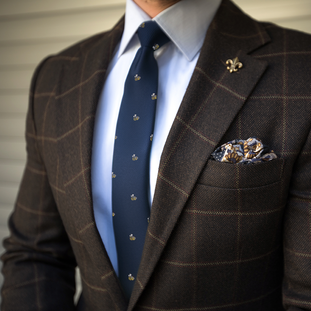 A stylish person dressed in a brown checkered suit with a light blue shirt, Bee Skinny Tie, and patterned pocket square exudes an unmistakable allure.