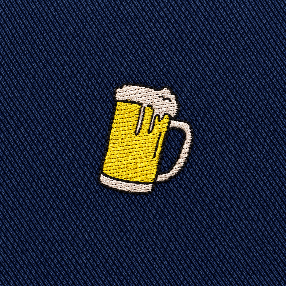 Embroidered patch of a frothy beer mug on dark blue diagonal fabric background, perfect for accenting the Beer Skinny Tie.