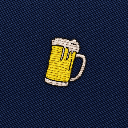 Embroidered patch of a frothy beer mug on dark blue diagonal fabric background, perfect for accenting the Beer Skinny Tie.