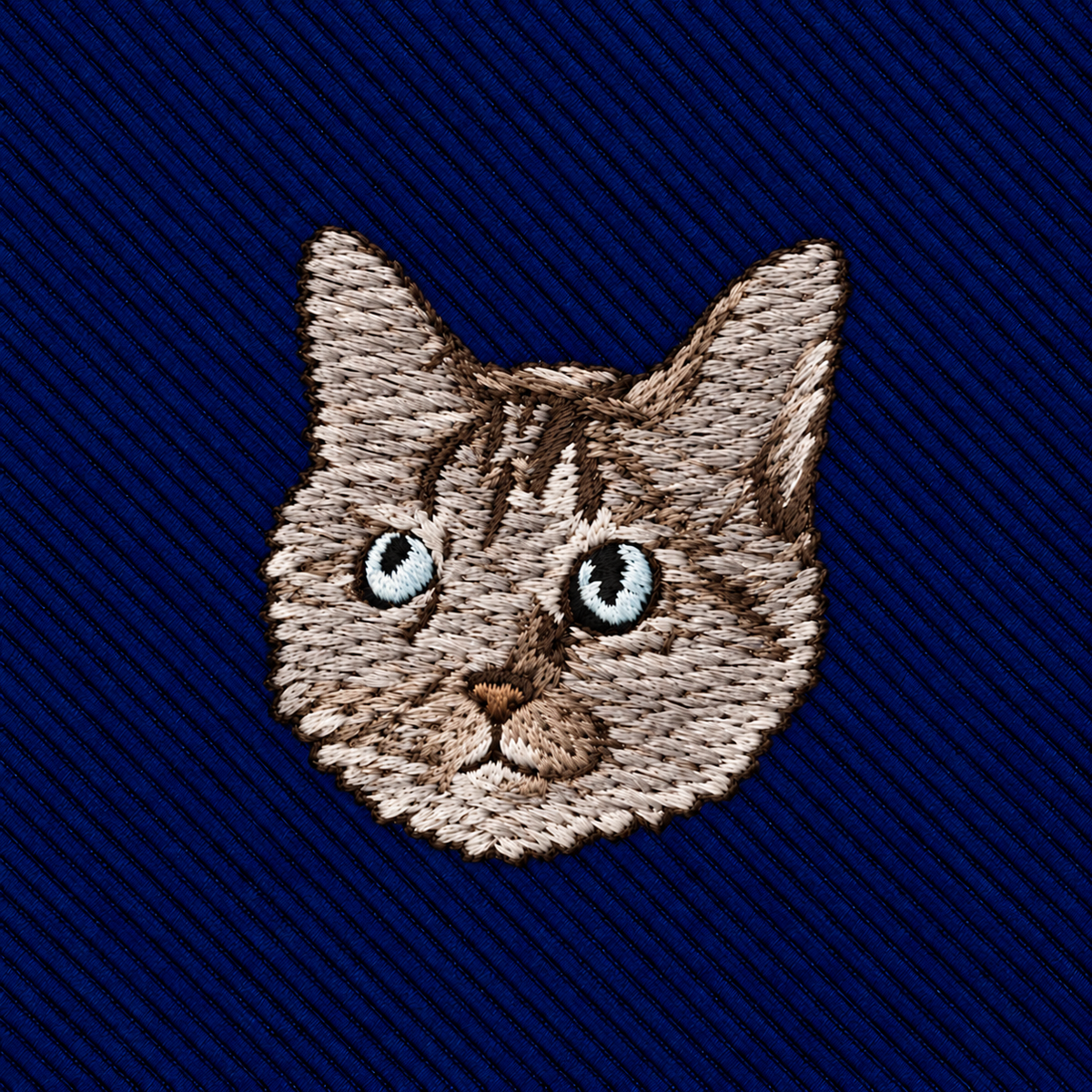 Cat Skinny Tie featuring an embroidered patch of a cat’s face with tabby markings and blue eyes on a dark blue ribbed background.