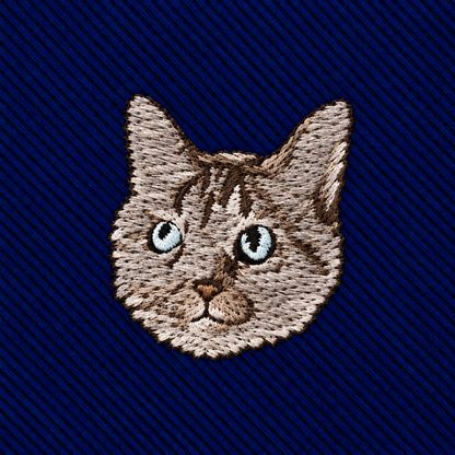 Cat Skinny Tie featuring an embroidered patch of a cat’s face with tabby markings and blue eyes on a dark blue ribbed background.
