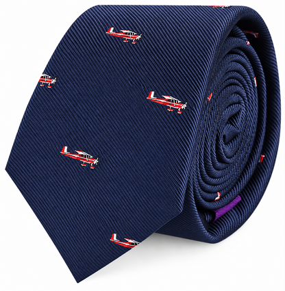 Classic Aircraft Skinny Tie in navy blue, adorned with a pattern of small red and white airplane illustrations, rolled up with the pointed end facing forward. This stylish aircraft print tie is a thoughtful gift for pilots or aviation enthusiasts.