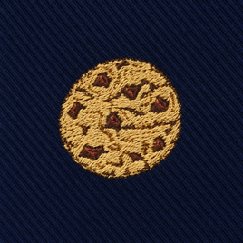 The Cookies Skinny Tie features a round, embroidered chocolate chip cookie motif on dark blue, diagonally ribbed fabric for a sweet, dessert-inspired look.