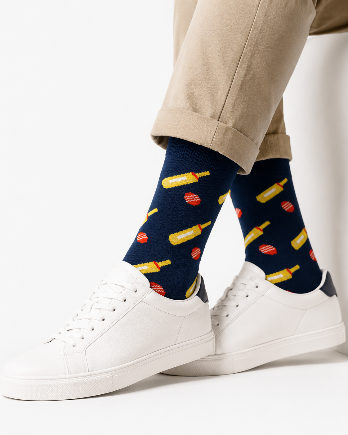 Person wearing light brown pants, white sneakers, and Cricket Bat & Ball Socks—navy blue socks with a playful yellow and red pattern, making great cricket gifts for any fan.