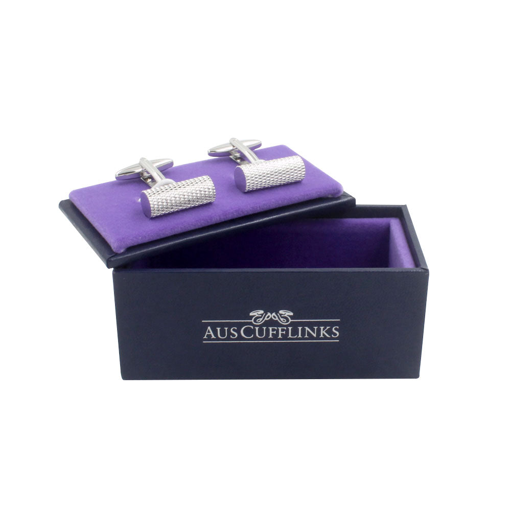 A pair of Cylinder Cufflinks with a polished silver finish displayed inside an open black box with a purple interior, branded "AUSCUFFLINKS" on the front, exuding rolling elegance.