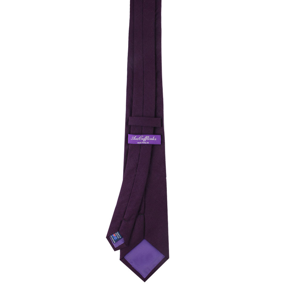 The Dark Purple Cotton Skinny Tie & Pocket Square Set features a dark purple tie with a lighter label and keeper loop, crafted from cotton for a sleek skinny fit, perfect against a crisp white backdrop.