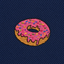 Donut Skinny Tie featuring an embroidered patch of a donut with pink icing and colorful sprinkles on dark blue, diagonal textured fabric—a fun dessert-themed accessory that makes the perfect gift for food lovers.