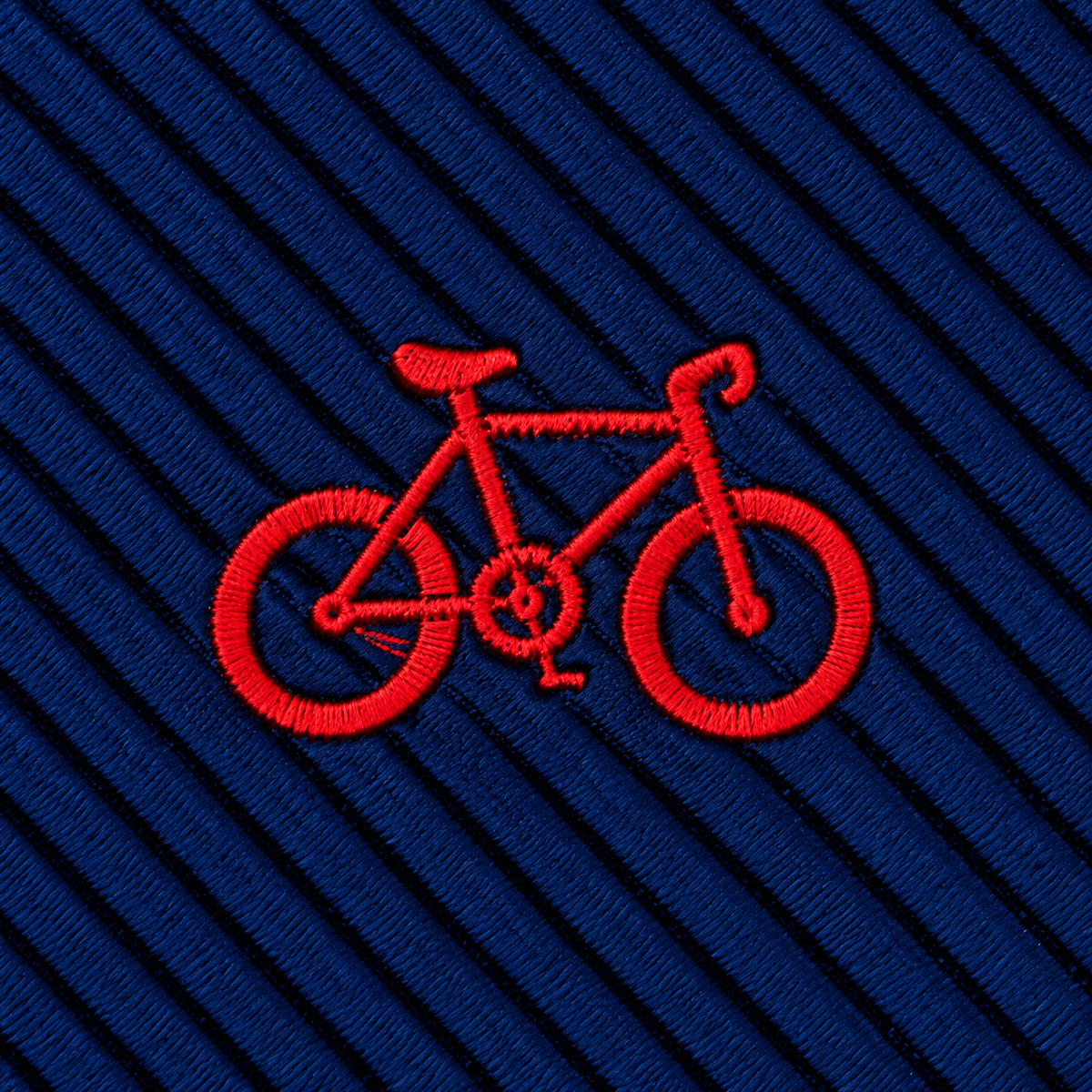 Introducing the Cyclist Skinny Tie: featuring a red embroidered bicycle on dark blue, diagonally ribbed fabric—a perfect choice for anyone seeking unique fashion accessories inspired by cycling.