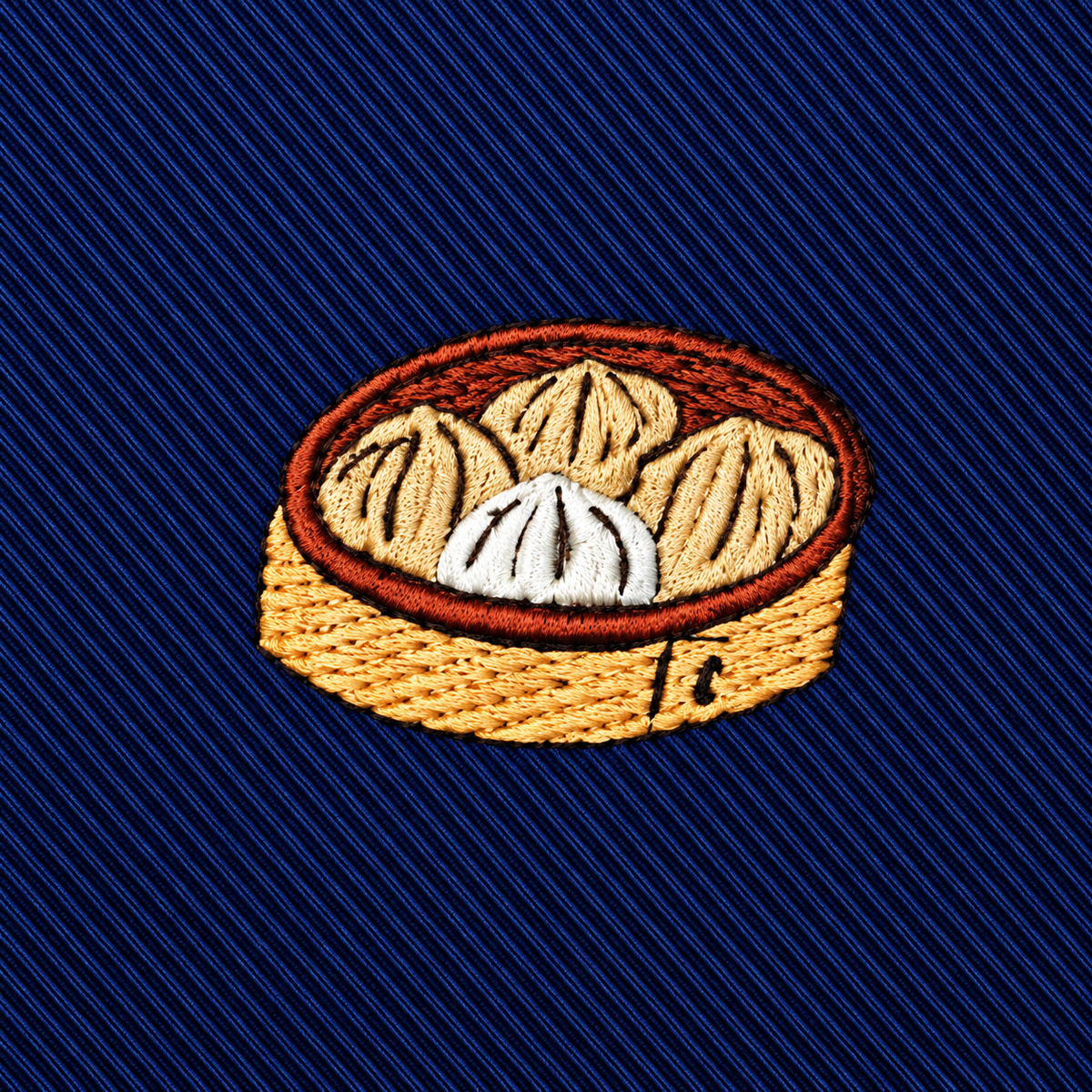 Introducing the Dumplings Skinny Tie—featuring an embroidered patch of four steamed dumplings nestled in a round bamboo basket, set against a dark blue diagonal striped background. This tie makes a perfect unique foodie gift or a playful addition to any dumpling lover’s wardrobe.