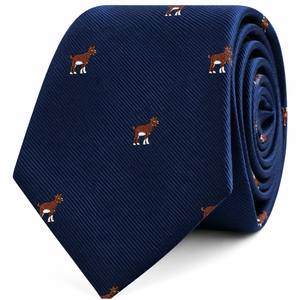 The Billy Goat Skinny Tie, shown rolled up neatly on a white background, features a navy blue design with a repeating pattern of small brown and white embroidered goats.