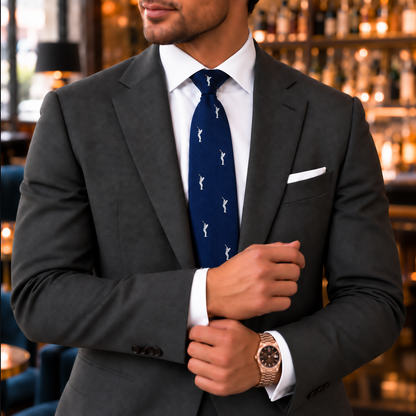 A man in a dark suit and white shirt stands in a bar, adjusting his cuff while wearing the Golf Swing Skinny Tie—a patterned navy blue skinny tie that makes the perfect golf gift—along with a stylish wristwatch.