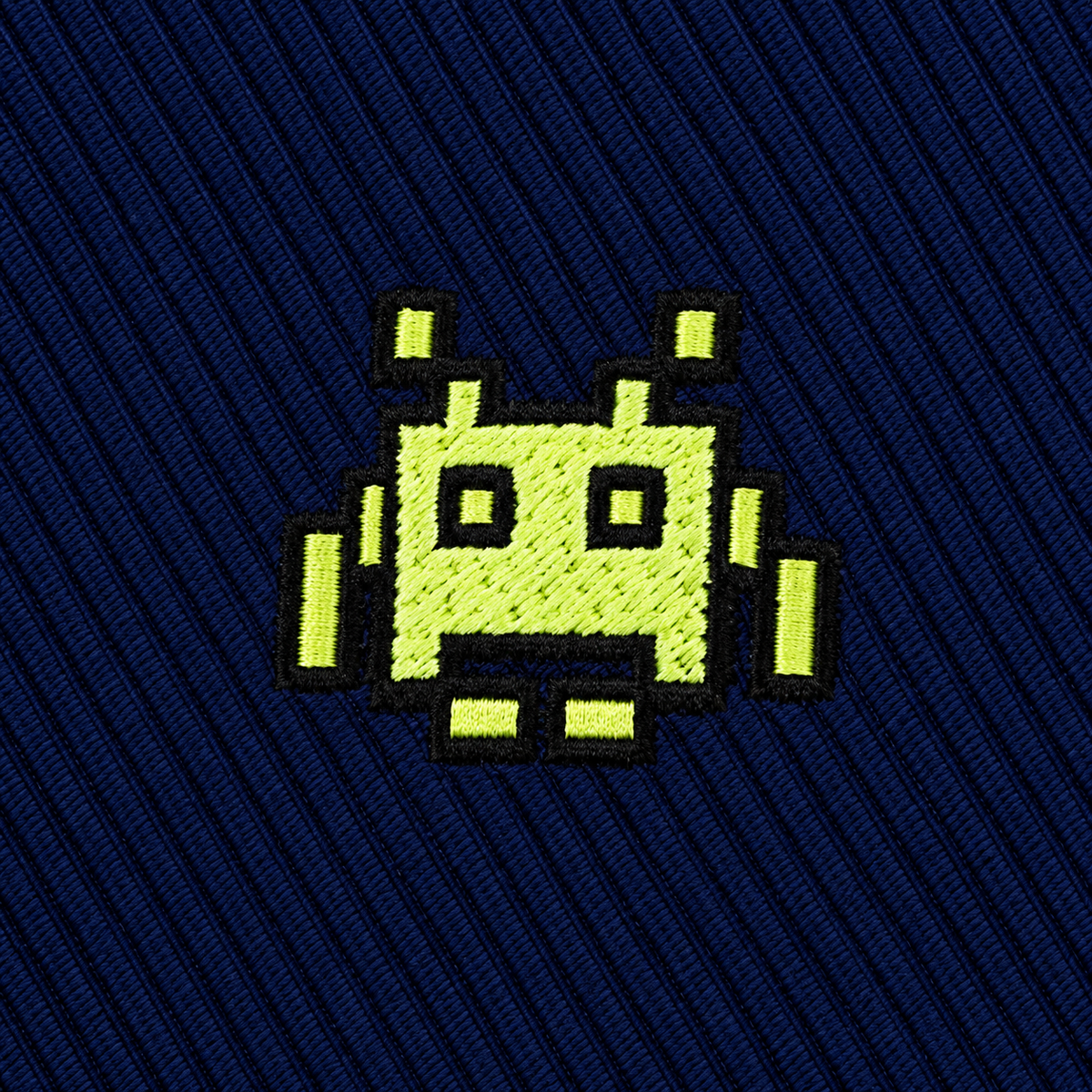 An embroidered lime green pixelated alien from a Green Space Invader Skinny Tie centered on a dark blue ribbed fabric.