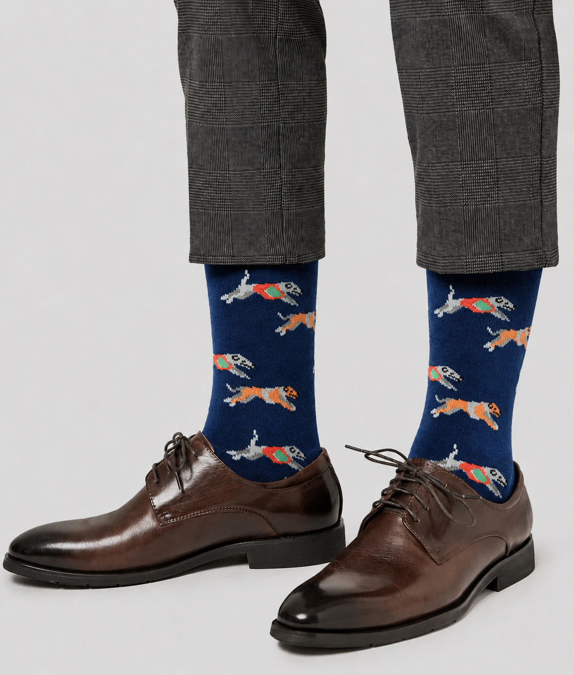 Person wearing brown dress shoes, grey plaid pants, and Greyhound Racing Socks with a flying dog pattern featuring capes and goggles.