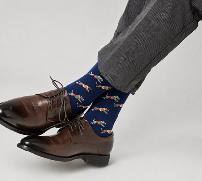 A person wearing brown dress shoes, gray plaid pants, and Greyhound Racing Socks with an orange fish pattern sits cross-legged.