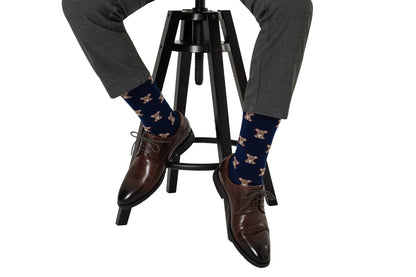 Person sitting on a black stool wears gray pants, brown shoes, and navy Koala Socks with an adorable style featuring a dog pattern.