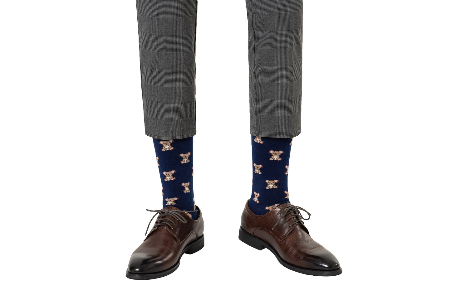 A person sporting an adorable style with gray pants, brown dress shoes, and charming blue Koala Socks with teddy bear patterns.