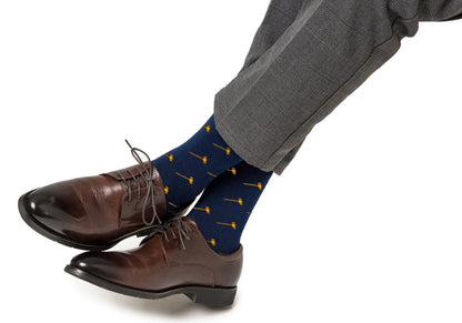 A person wearing gray plaid trousers, brown leather dress shoes, and Gavel Socks—navy blue legal-themed socks with a small yellow gavel pattern.