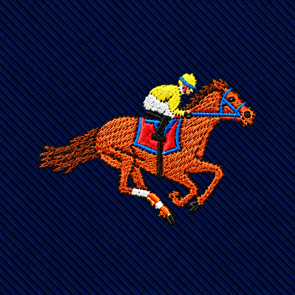 Embroidered patch of a jockey in a yellow and white shirt riding a brown racehorse on a dark blue ribbed background, featured on a Melbourne Race Horse Skinny Tie.