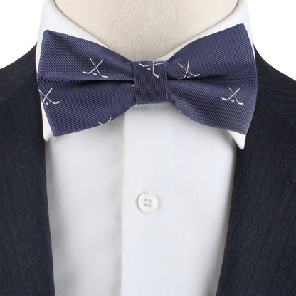 A close-up of a person wearing the Ice Hockey Cross Bow Tie with blue fabric, white embroidered crossed golf clubs, a white dress shirt, and a dark pinstriped suit jacket for a sporty touch.
