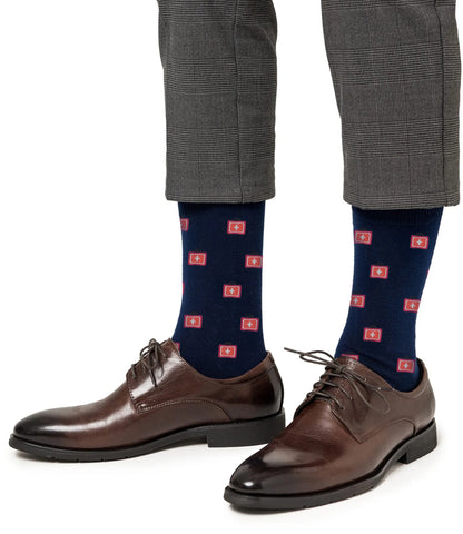 A person wearing brown dress shoes, gray plaid pants, and Medical Cross Socks in navy blue with a red cross pattern.