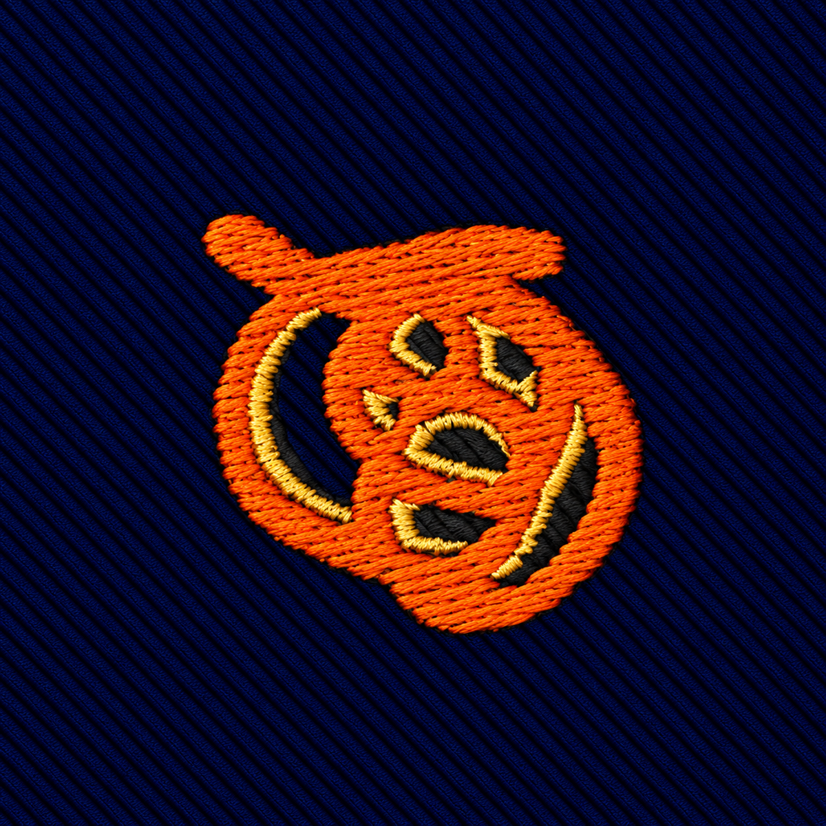 An embroidered orange jack-o’-lantern on a dark blue diagonal-striped Pretzel Skinny Tie.