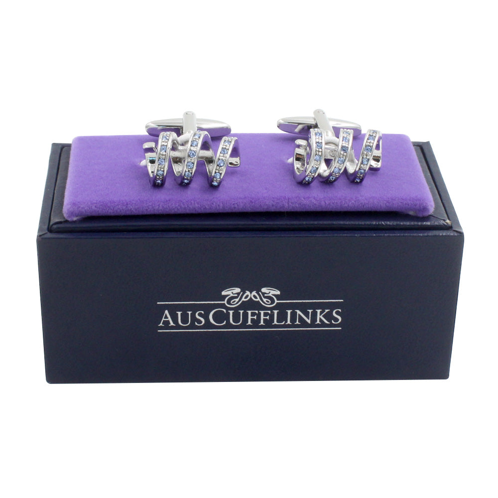 A pair of Blue Stone Twirl Cufflinks with an elegant spiral twist, showcased on a plush purple velvet cushion atop a black box labeled "AUSCUFFLINKS.