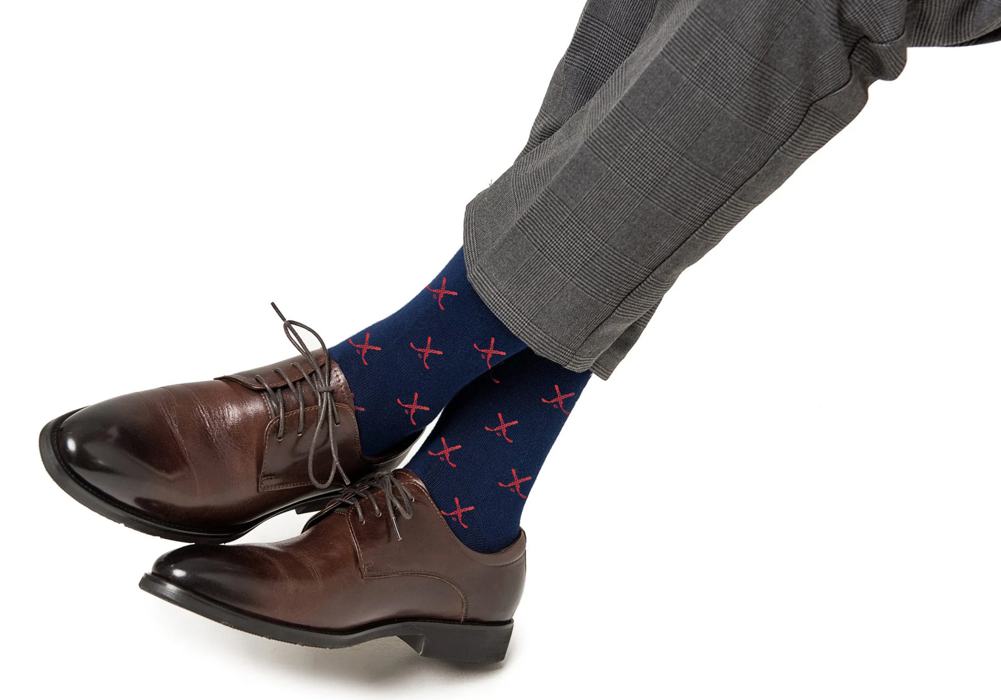 A person wearing brown dress shoes, gray plaid pants, and Red and Navy Ice Hockey Cross Socks with feet crossed against a white background.