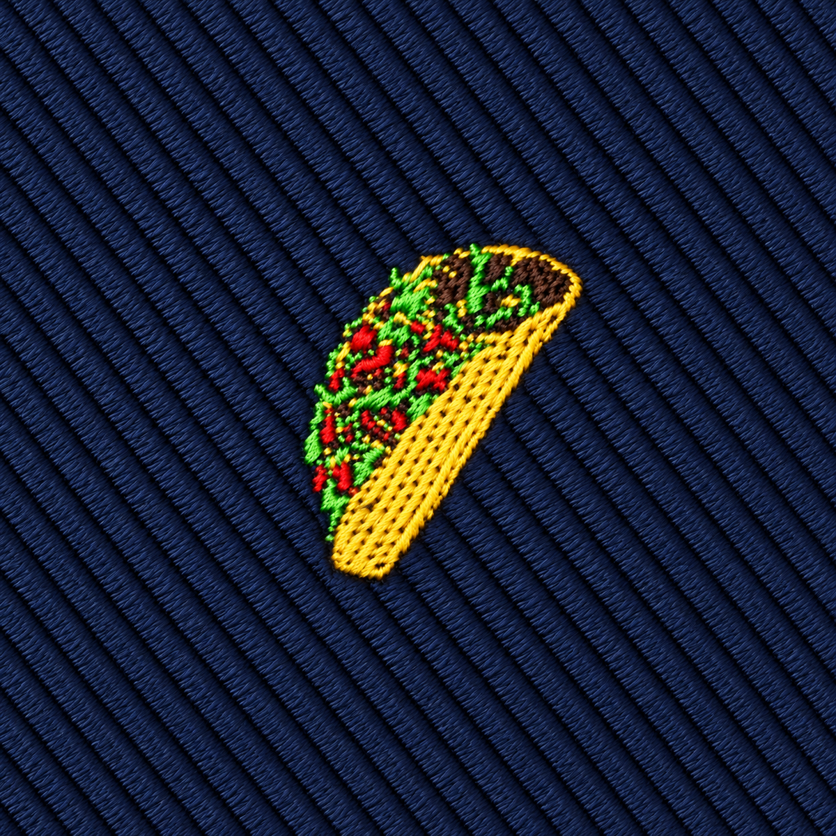 Embroidered yellow taco with meat, lettuce, and tomato on a dark blue diagonal striped fabric background makes the Taco Skinny Tie a perfect addition to any fun taco print or food-inspired necktie collection.