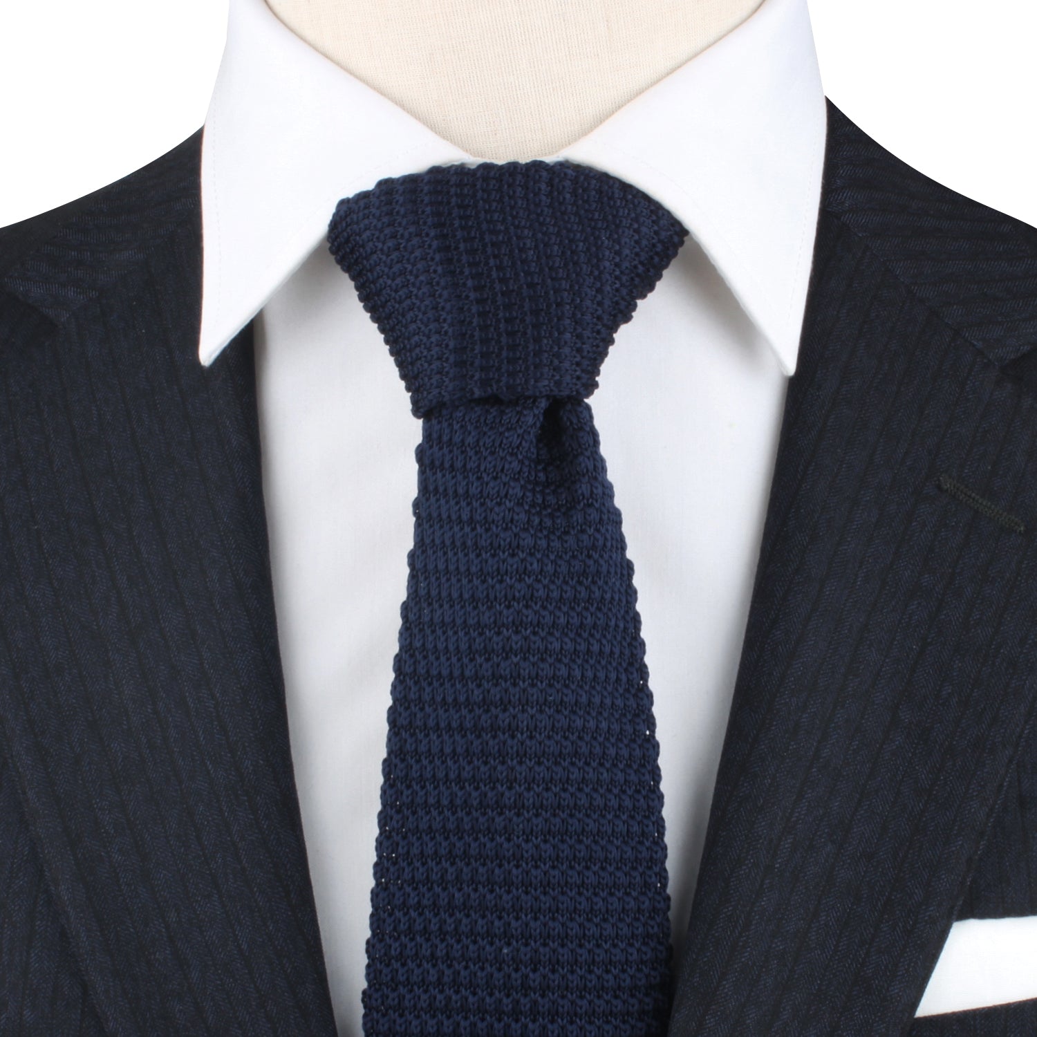 Close-up of a person wearing a dark pinstripe suit jacket, a white dress shirt, and a Navy Knitted Skinny Tie, exuding elegance with its intricate weave pattern.