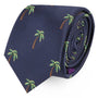 The Palm Tree Skinny Tie is a dark blue accessory adorned with a pattern of small, embroidered green palm trees, exuding a tropical allure.