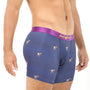 A man stands confidently, showcasing his Goat Underwear blue boxer briefs adorned with dog prints and a striking purple waistband. Visible tattoos decorate his torso, adding to the aura of mountainous comfort he exudes.