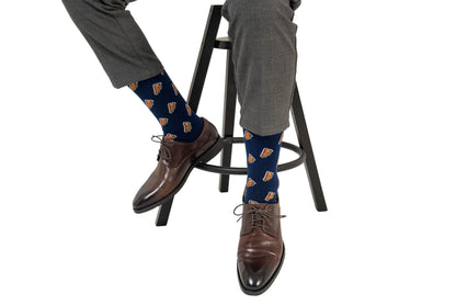 Person wearing gray trousers, Pizza Socks with a blue base and a pizza slice pattern, and brown lace-up shoes, sitting on a high chair in comfort and style.