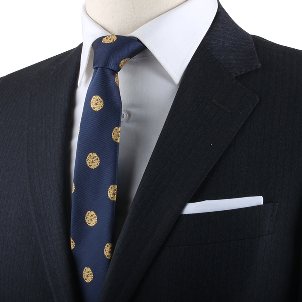 Close-up of a person wearing a white dress shirt, a dark suit jacket with a pocket square, and the Cookies Skinny Tie showcasing timeless style with its blue fabric adorned with yellow circular patterns.