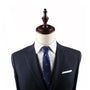 A mannequin dressed in a dark suit with a Triceratops Skinny Tie featuring a pattern, white dress shirt, and a white pocket square exudes modern elegance against a plain white background.