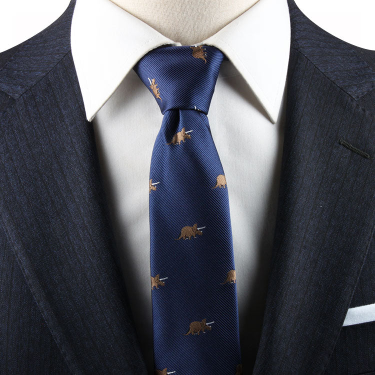 Close-up of a person wearing a dark pinstripe suit with a white dress shirt and a Triceratops Skinny Tie featuring a pattern of small brown triceratops, blending prehistoric charm with modern elegance.