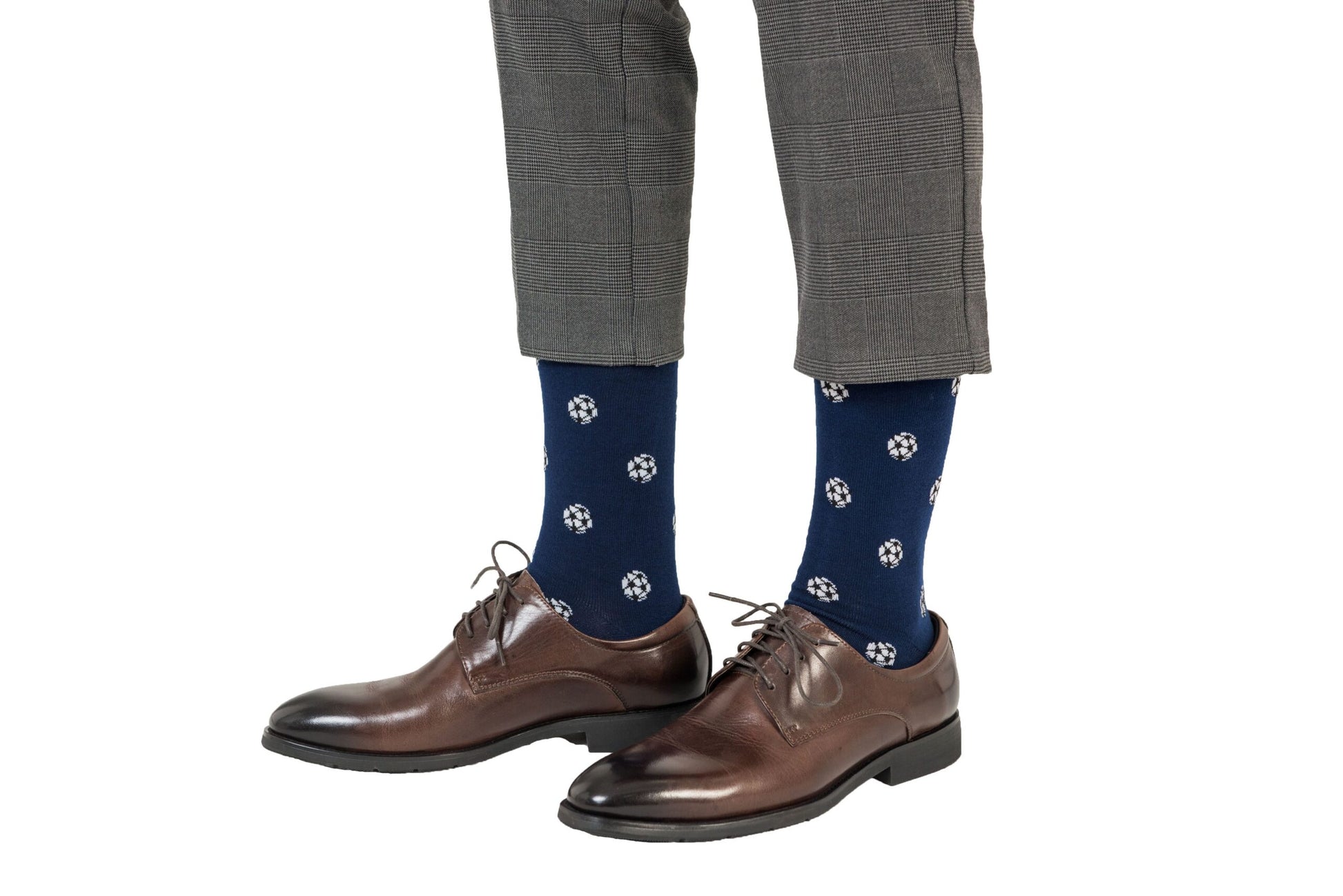 Man wearing gray checked pants, blue Soccer Socks with white circular patterns, and brown leather dress shoes that promise goal-worthy comfort with every step.