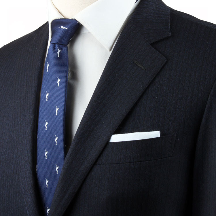 Close-up of a person wearing a dark suit, white dress shirt, and a Golf Swing Skinny Tie with white patterns that subtly hint at a golf motif. A white pocket square is tucked into the suit's breast pocket.